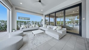 A modern living room with a sectional sofa, a coffee table, and a large sliding glass door leading to a pool area. - 9BR Reunion Mansion | Pool, Spa & Home Theater (Kissimmee)