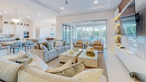 A spacious living area with a modern kitchen, large windows, and a ceiling fan. - 9BR Reunion Mansion | Pool, Spa & Home Theater (Kissimmee)