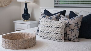Une chambre à coucher avec un lit, une table de chevet avec une lampe, un élément de décoration murale et une fenêtre avec des stores.