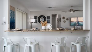 Une cuisine dotée d’un îlot central, de tabourets de bar blancs et d’un ventilateur de plafond.