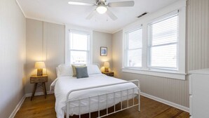 Una camera da letto con un letto, due comodini con lampade, una ventola a soffitto e due finestre con tende.