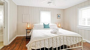 Une chambre avec un lit blanc, un plancher en bois, un ventilateur de plafond et deux lampes de chevet.