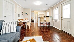 Un salon spacieux avec un canapé, un coin repas avec des chaises et une cuisine équipée d’un réfrigérateur et de tabourets de bar.