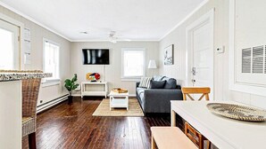 Un salon moderne avec un plancher en bois, un canapé gris, une table basse blanche et un coin repas comprenant un banc et une table.