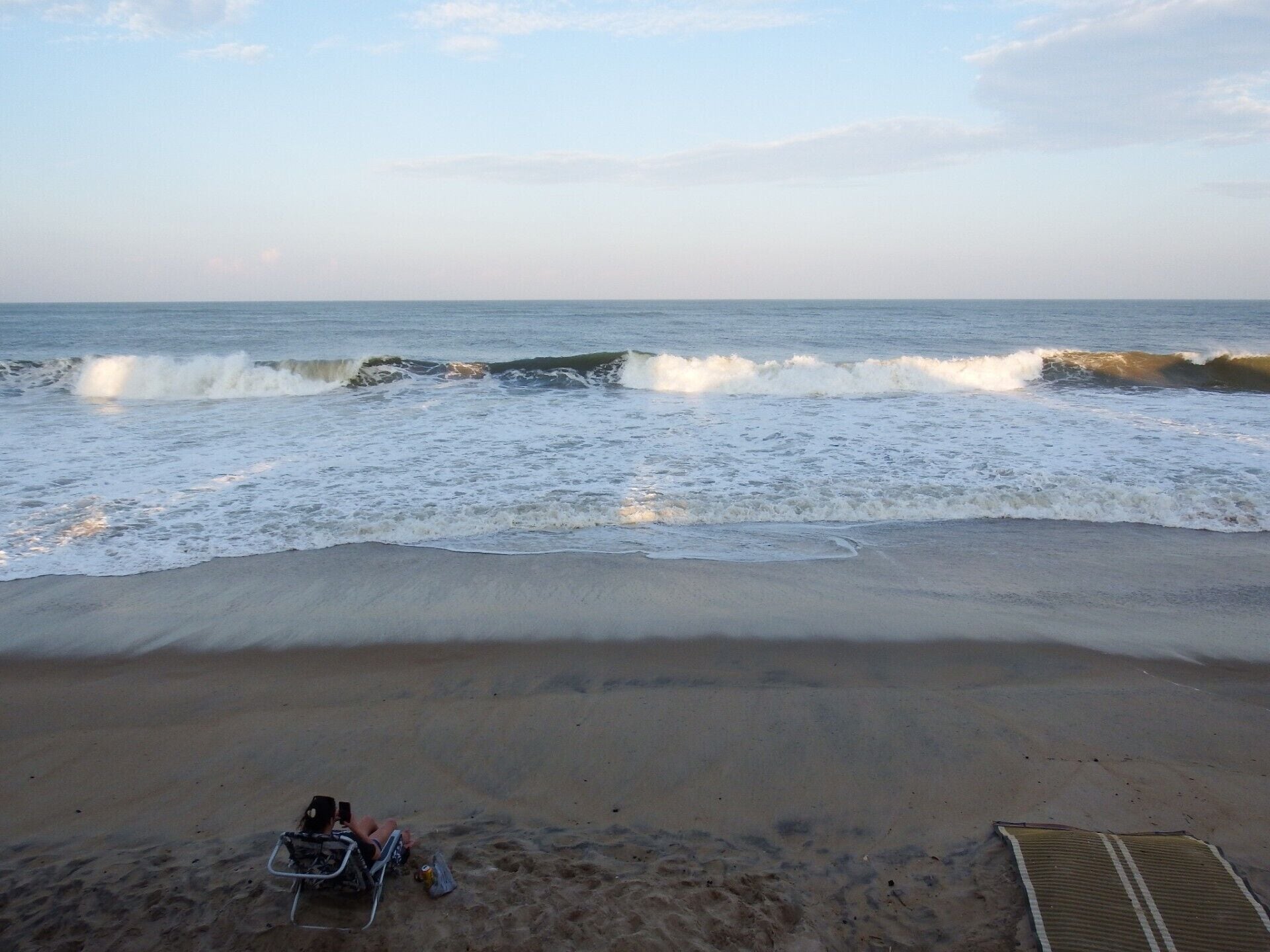 Une plage où les vagues déferlent sur le rivage, une personne assise sur une chaise de plage et un parasol de plage.