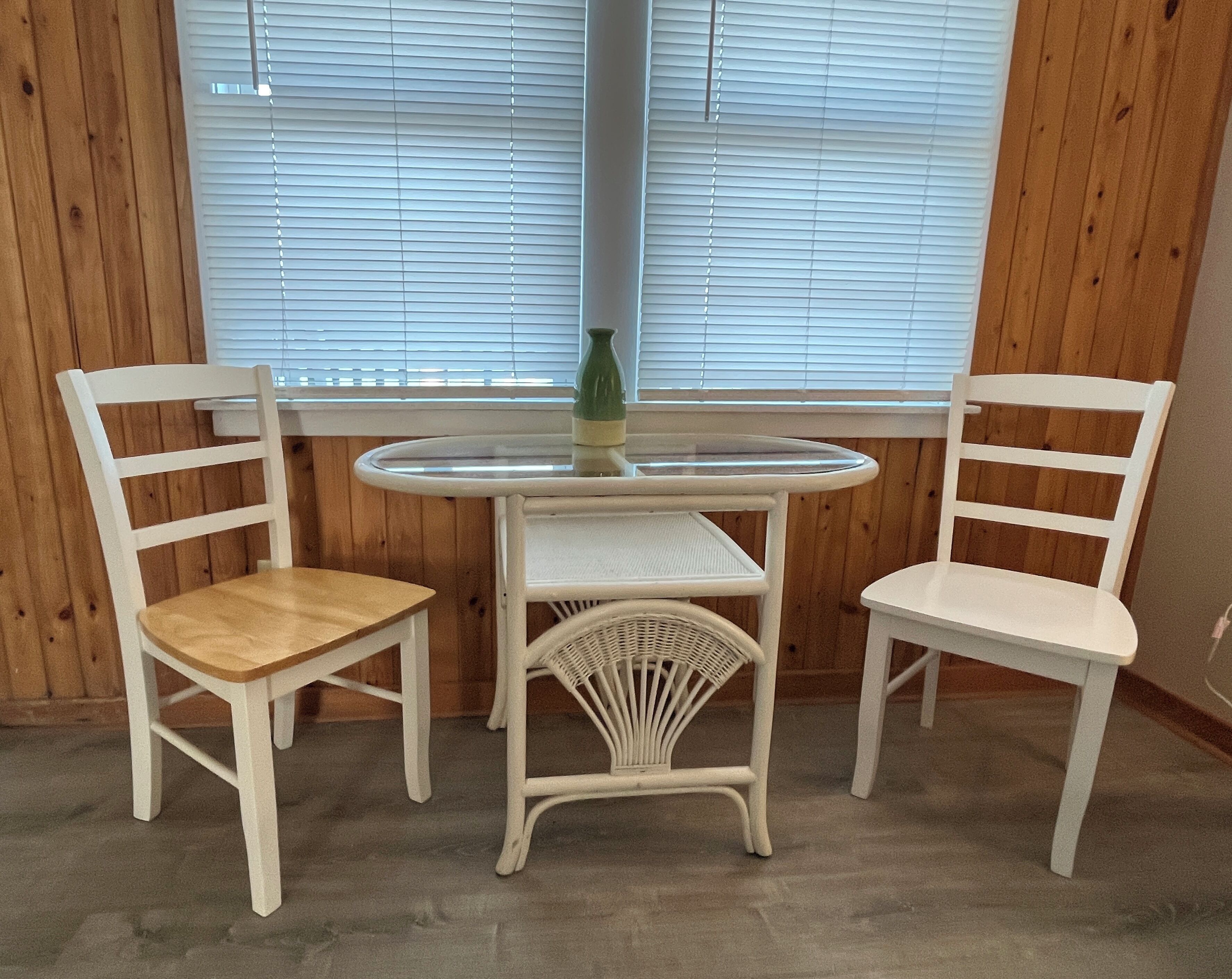 Una habitación con dos sillas blancas, una mesa redonda pequeña y una ventana con persianas.