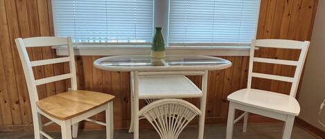 A room with two white chairs, a small round table, and a window with blinds.