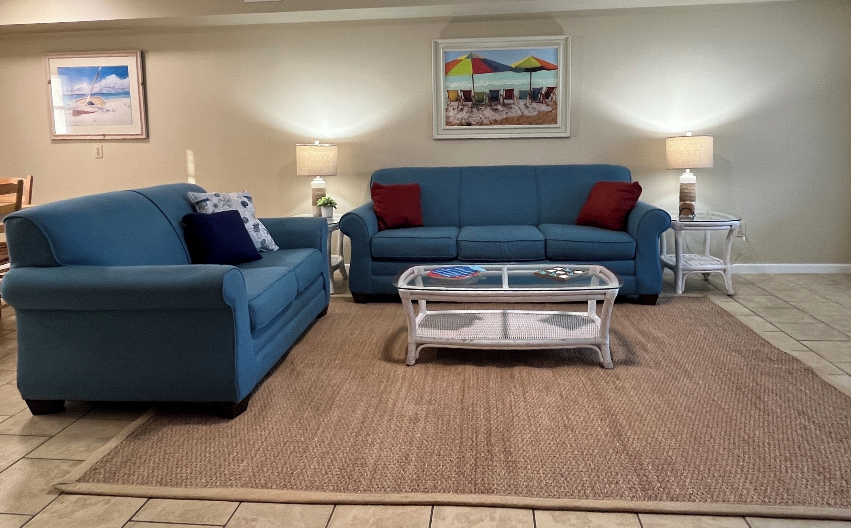 A living room with two blue sofas, a glass coffee table, and a beige carpet.