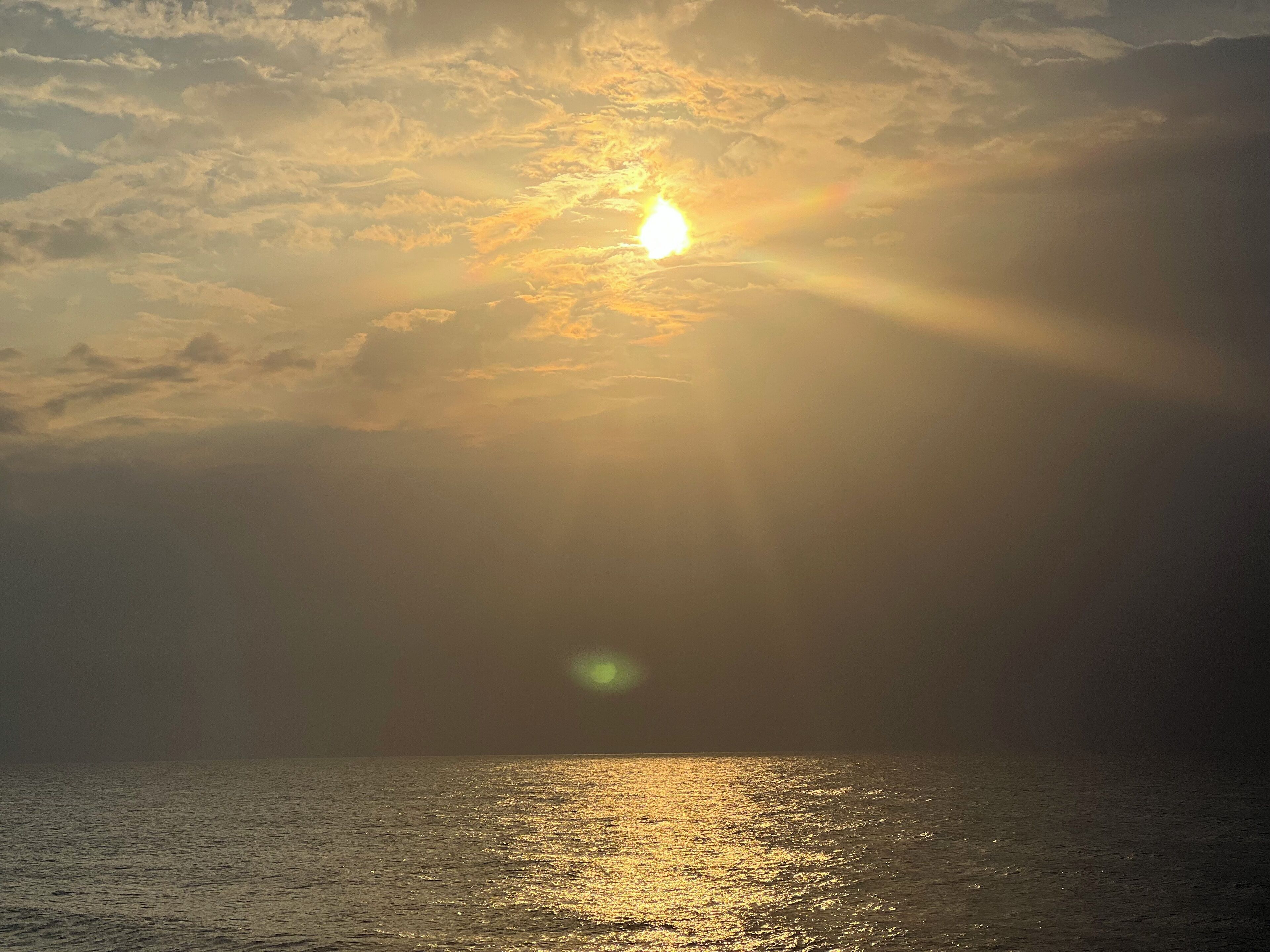 Een zonsondergang boven het water, met zonlicht dat op het oppervlak weerkaatst.