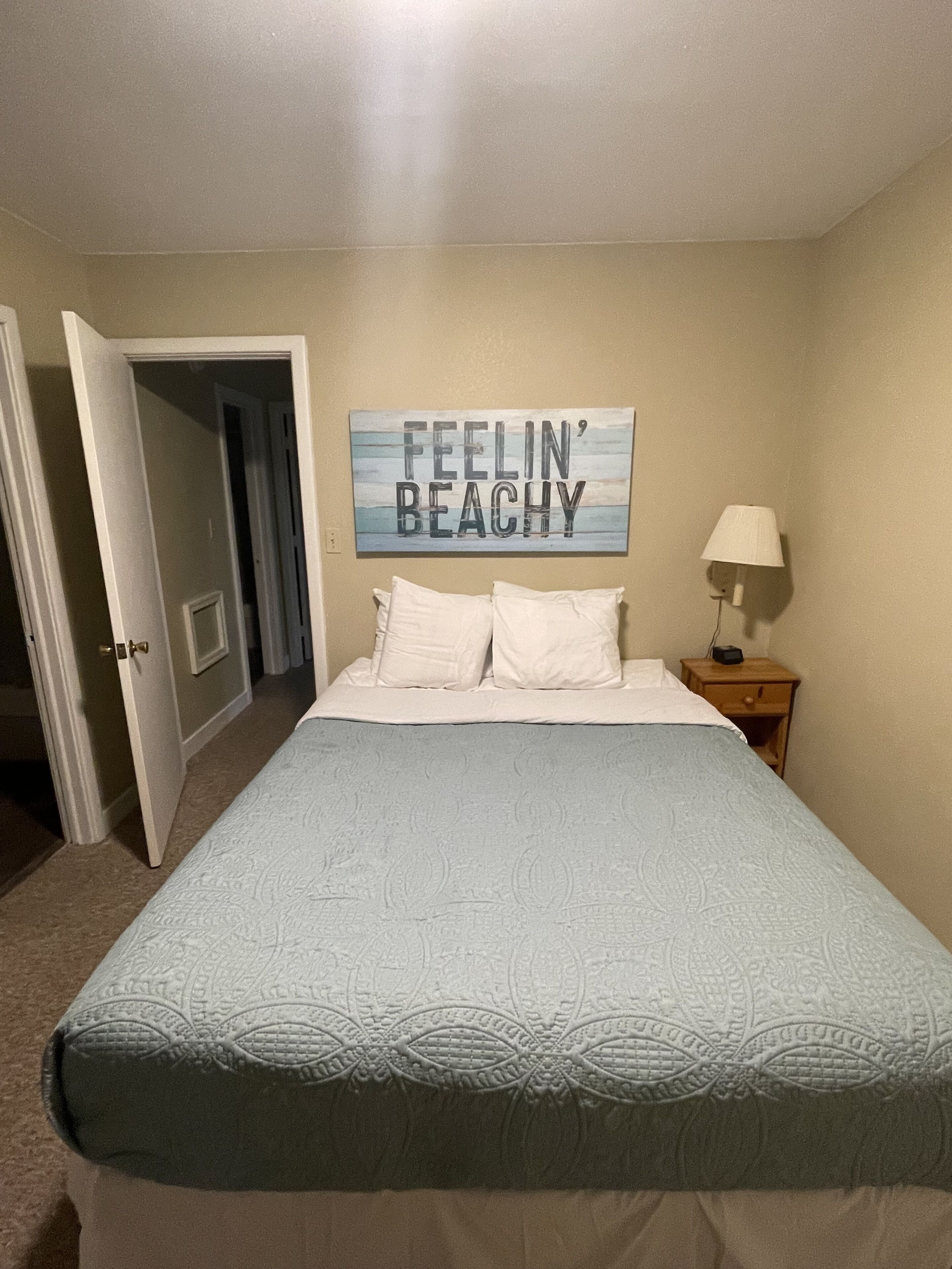 A bedroom with a bed, a nightstand, a lamp, and a door leading to another room.