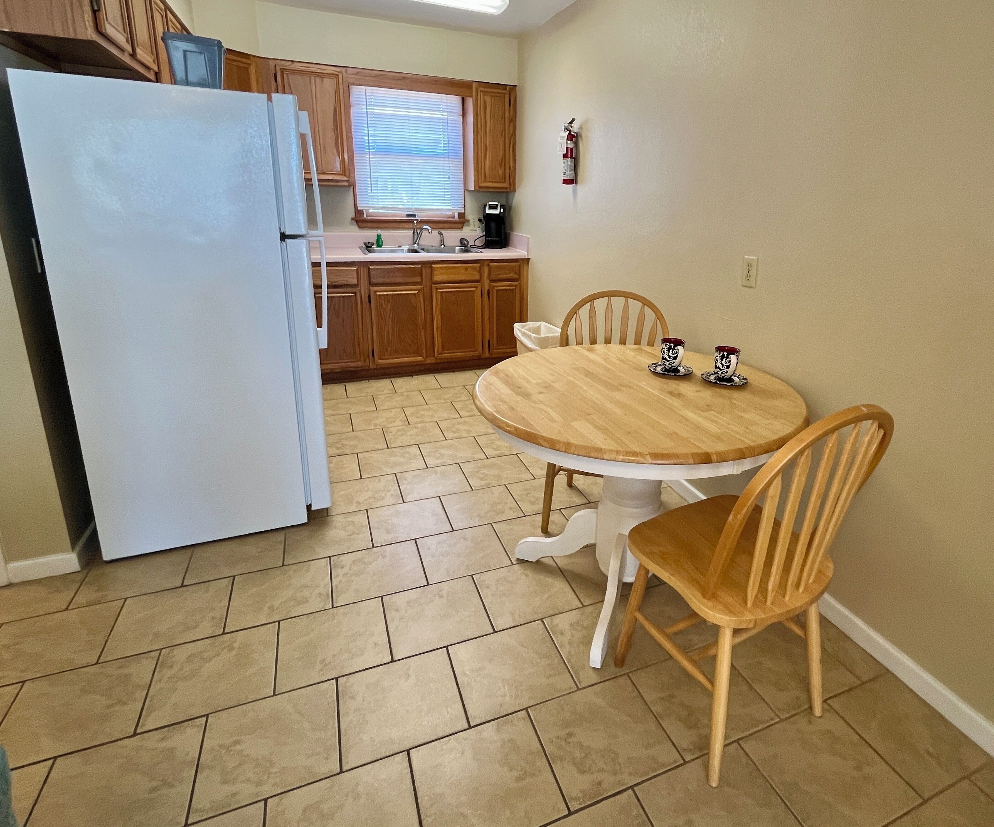 A compact kitchen with a refrigerator, wooden cabinets, a sink, and a round dining table with chairs.