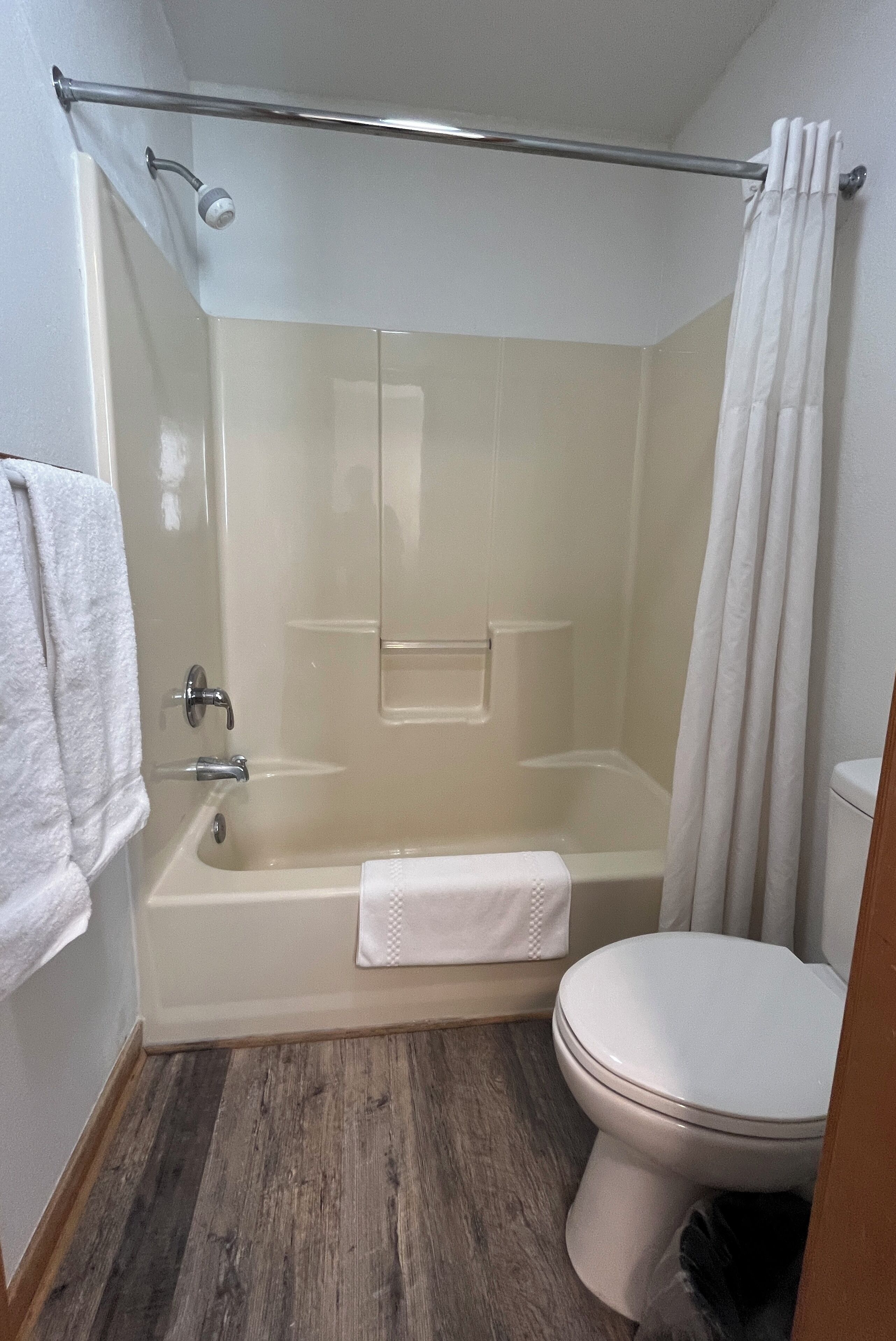 Un baño con ducha envuelta en vidrio, inodoro blanco y suelo de madera.