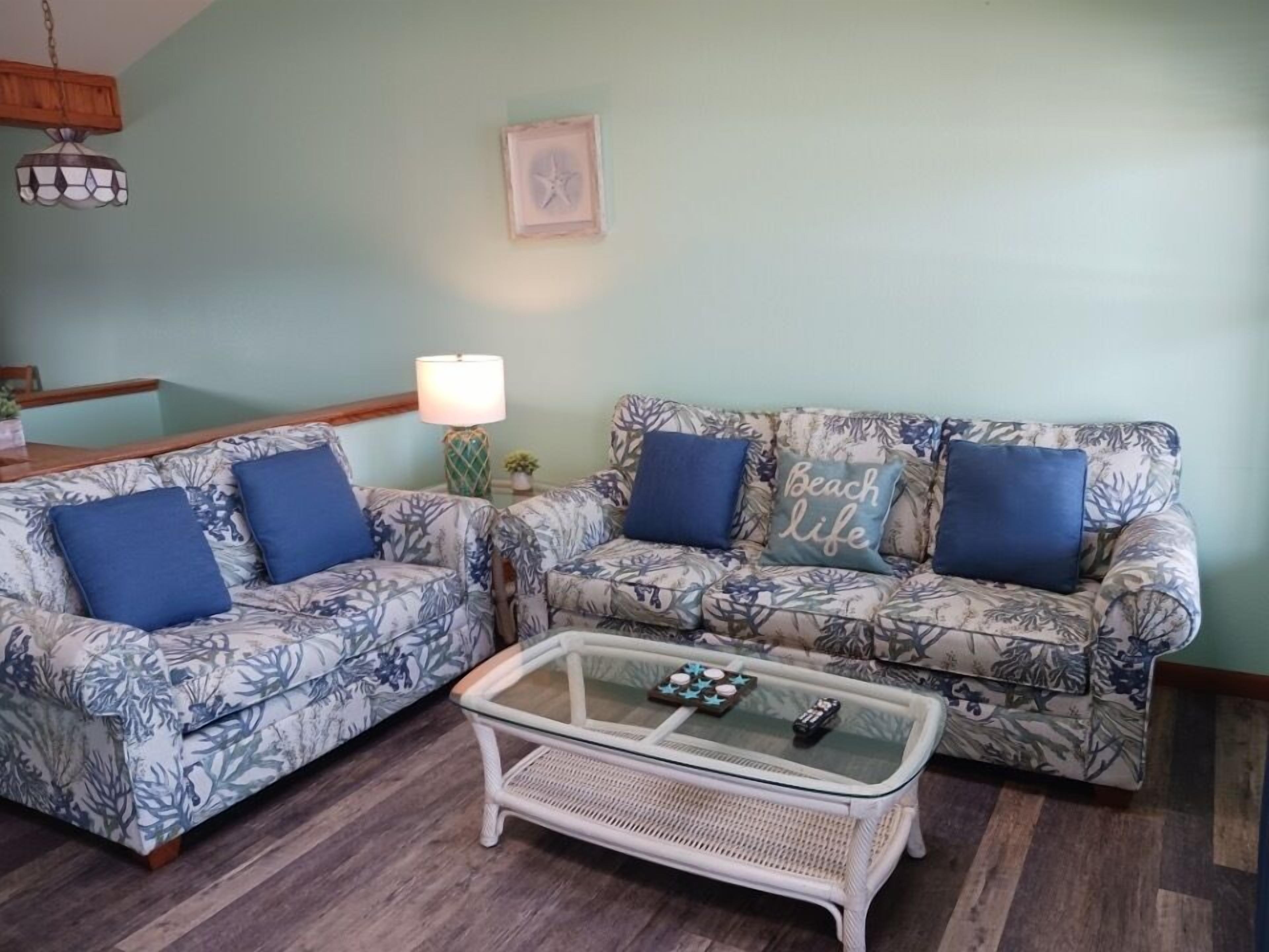 A living room with two patterned sofas, a glass coffee table, and a lamp.