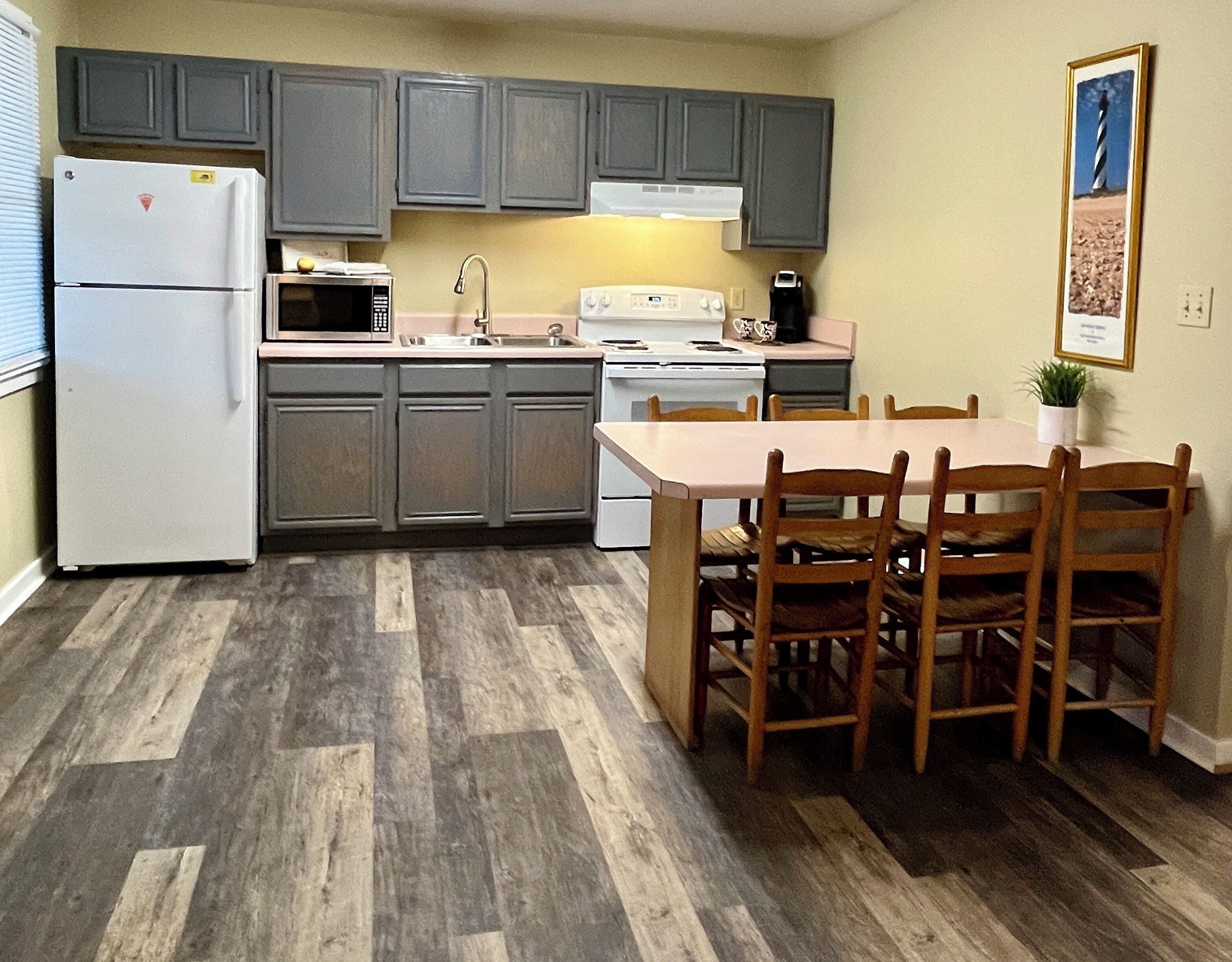 A kitchen with grey cabinets, a white refrigerator, a microwave, a sink, a stove, and a dining table with chairs.