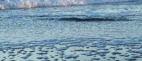 A beach with waves crashing onto the shore and a clear sky above.