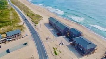 Vista aérea de una zona costera con una carretera, playa y varios edificios con techos oscuros.