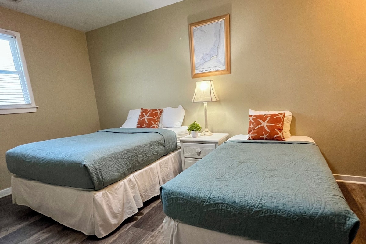 Une chambre avec deux lits, une table de chevet avec une lampe et une carte encadrée accrochée au mur.