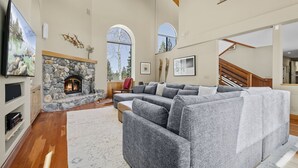 Ein großzügiges Wohnzimmer mit Kamin aus Stein, einem Ecksofa und einem großen Fernseher.