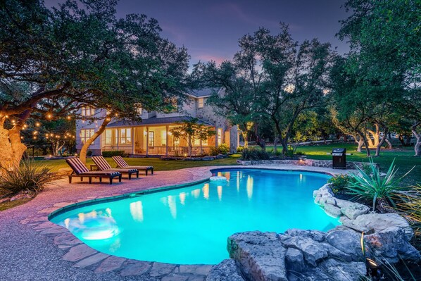 A swimming pool with a stone border, surrounded by lounge chairs and a stone wall.