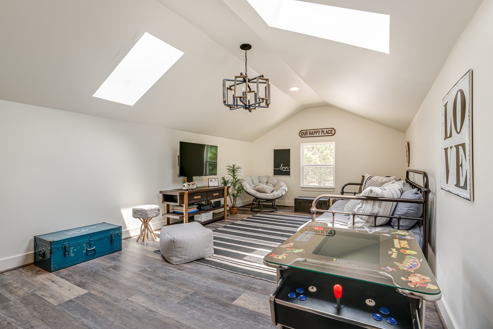 A spacious room with a loft bed, a play area with a table and chairs, a large window, and a ceiling light fixture.