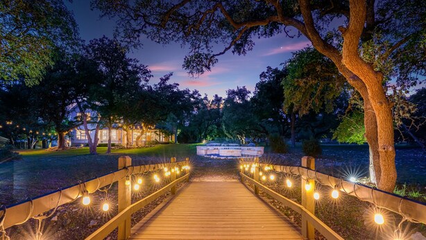 Un chemin en bois, illuminé par des guirlandes lumineuses, mène à un bâtiment sur lequel est apposée une enseigne.
