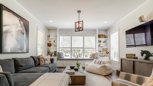 Uma sala de estar moderna com um sofá, poltrona e um banco perto de uma janela grande.
