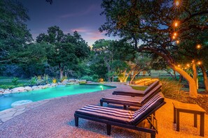 A pool area with lounge chairs and string lights.