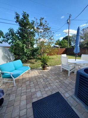 A patio area with a blue outdoor sofa, a white table and chairs, and a potted plant. - Your Perfect Getaway 4 bedroom residential home (Port St Lucie)