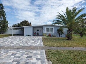 A single-story house with a covered porch, a paved driveway, and a well-maintained lawn. - Your Perfect Getaway 4 bedroom residential home (Port St Lucie)