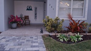 Een huis met een overdekte veranda, een bord met een welkomstdrankje en genummerde ramen.