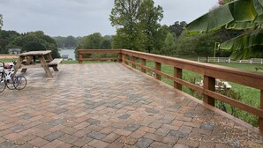 Une terrasse en bois avec une table de pique-nique et un vélo, donnant sur un lac et une végétation luxuriante.