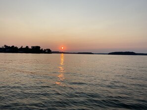 Een zonsondergang boven een rustig wateroppervlak met verre landmassa's.