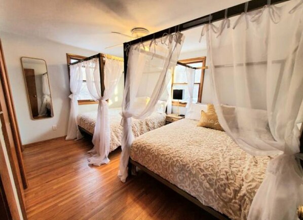 A bedroom with two beds, each with a canopy, wooden flooring, and a bedside table with a lamp. - New Sauna! St Paul, Mall of America, Spacious, Pool Table, Foosball Table (Saint Paul)