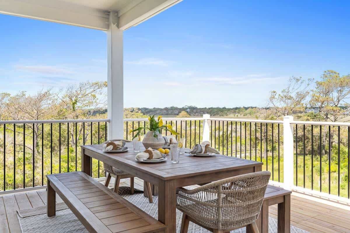 A covered outdoor dining area with a table set for two, surrounded by a white railing, overlooking a natural landscape.