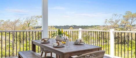 A covered outdoor dining area with a table set for two, surrounded by a white railing, overlooking a natural landscape.