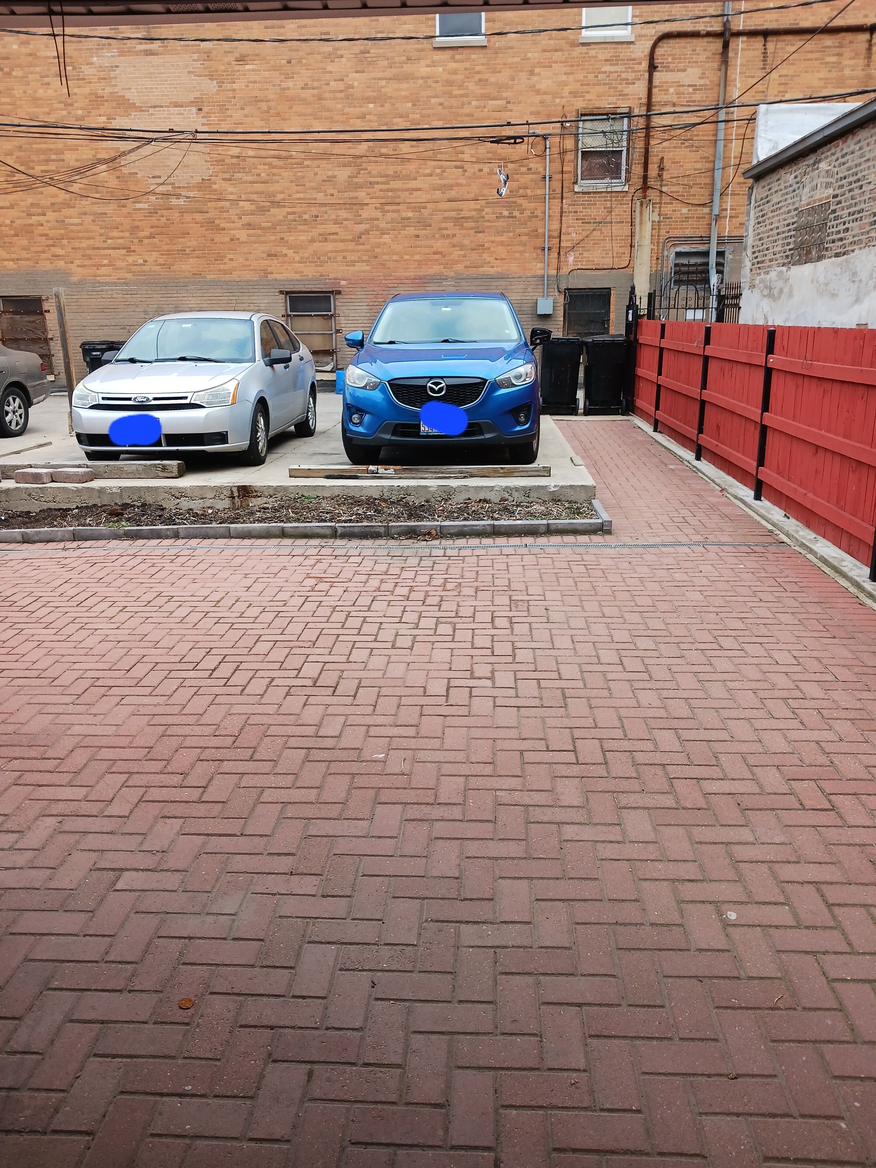 A parking area with two cars, a brick pavement, and a red fence.