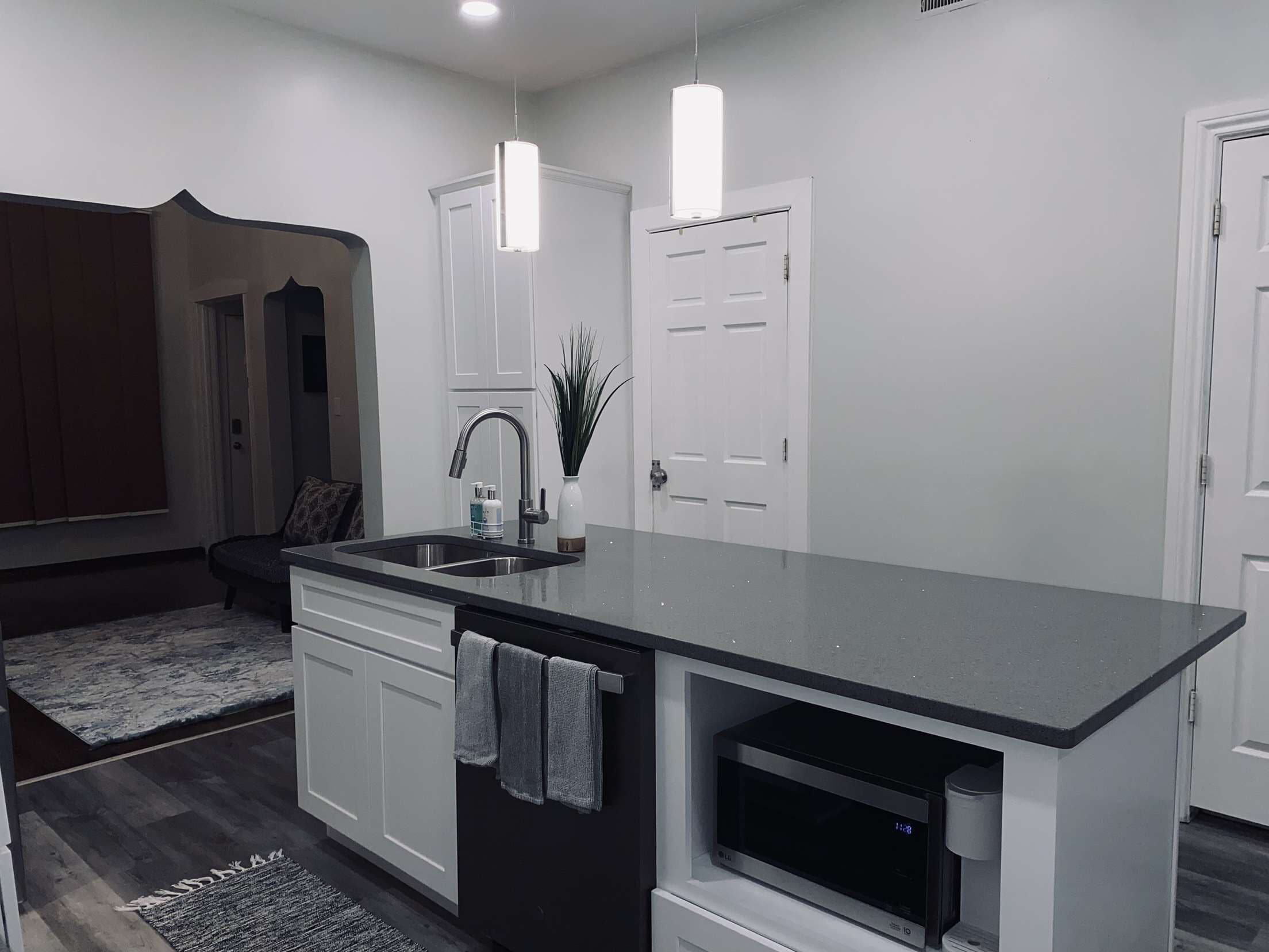 A modern kitchen with white cabinetry, a black countertop, a built-in microwave, and pendant lighting.
