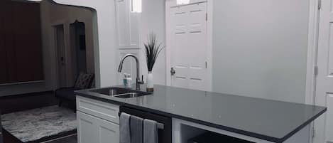 A modern kitchen with white cabinetry, a black countertop, a built-in microwave, and pendant lighting.