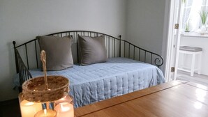 A bedroom with a bed, pillows, a bedside table with candles, and a view of a kitchen area.