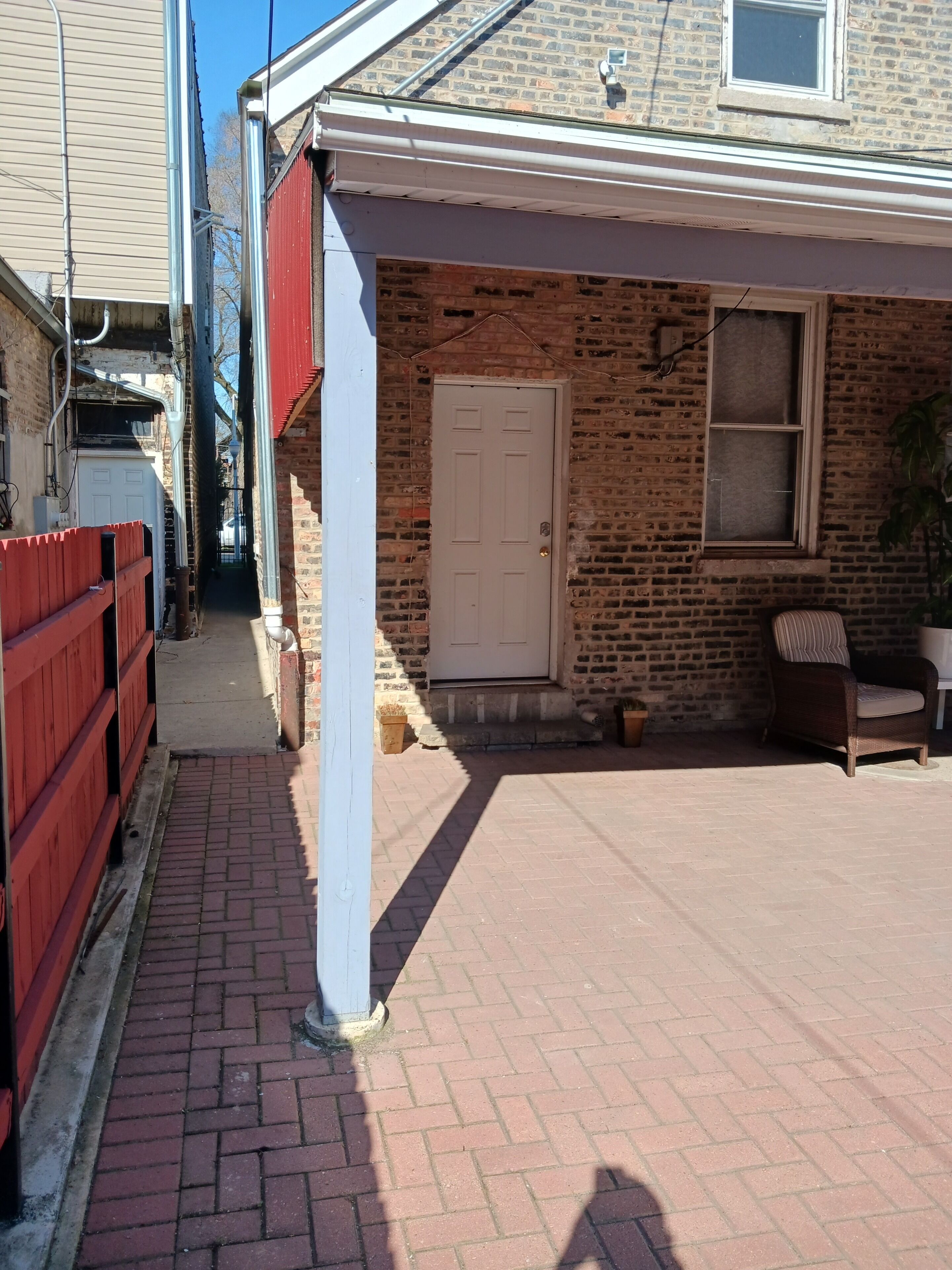 A brick house with a white door, a red fence, and a brick patio.