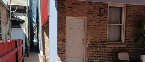 A brick house with a white door, a red fence, and a brick patio.