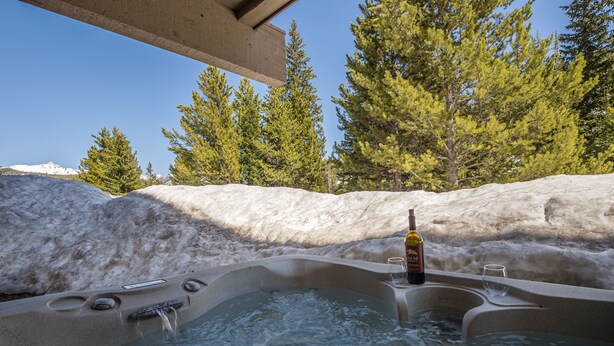 Un jacuzzi con una botella y un vaso, rodeado de nieve y árboles.