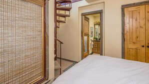 Un dormitorio con cama, una puerta de madera, un espejo y una escalera.
