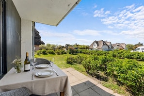 Un espacio de comedor al aire libre con una mesa preparada para dos personas, una botella de vino y un jarrón de flores.