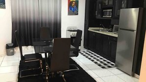 Une cuisine moderne avec des meubles noirs, un réfrigérateur en acier inoxydable, un four à micro-ondes et une cuisinière à gaz. On y trouve une table à manger avec des chaises et un tapis noir.