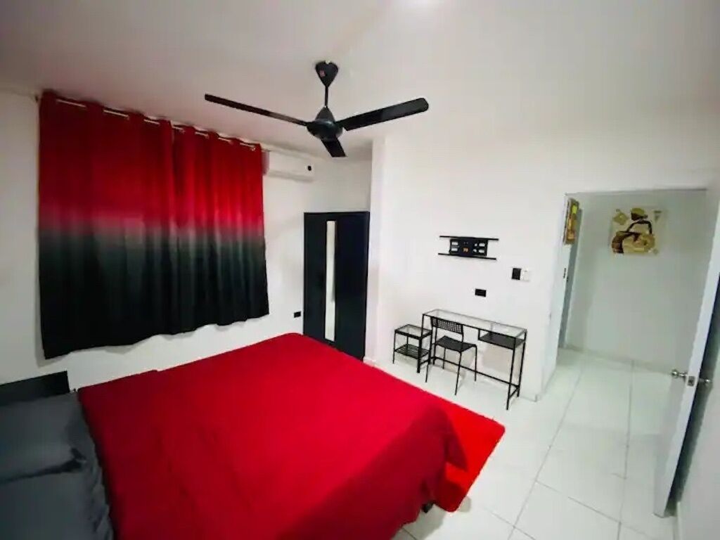 Een slaapkamer met een bed, een bureau en een plafondventilator.