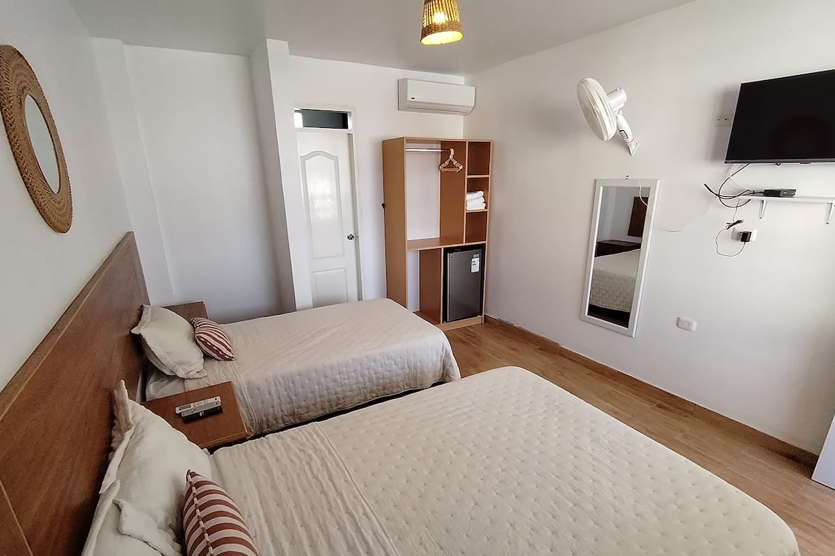 A hotel room with two beds, a wardrobe, a TV, and a small fridge.
