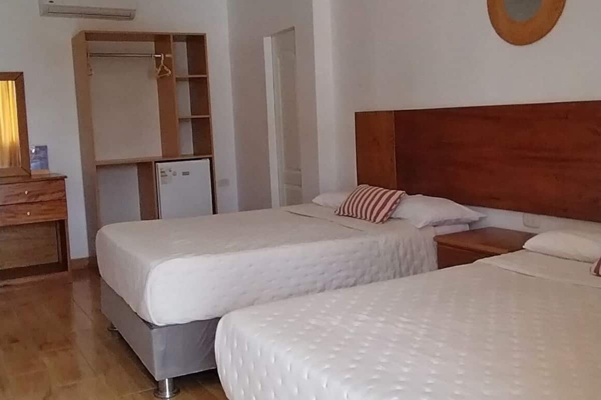 A hotel room with two beds, a wooden headboard, a small bedside table, a mirror on the wall, and a hanging light fixture.