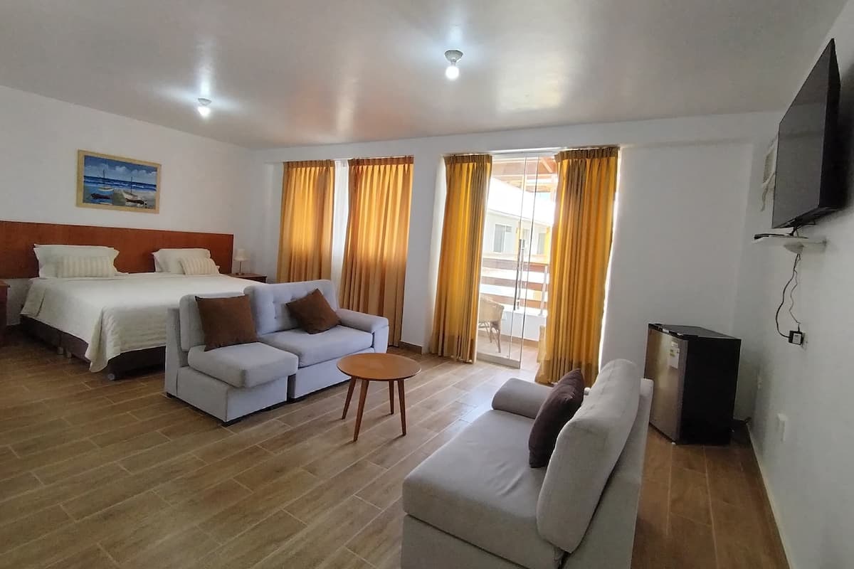 A hotel room with a bed, a sofa, a small table, and a TV.