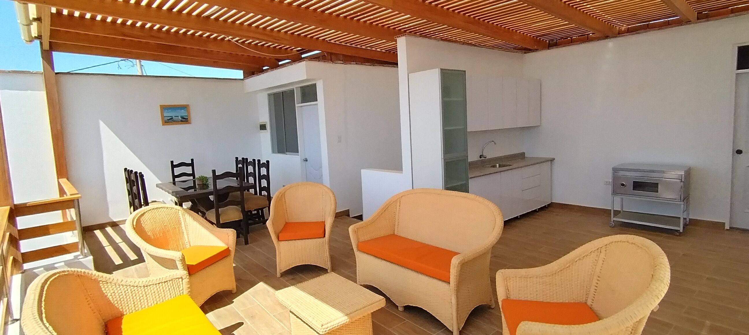 A room with wicker furniture, a dining table, and a kitchenette.